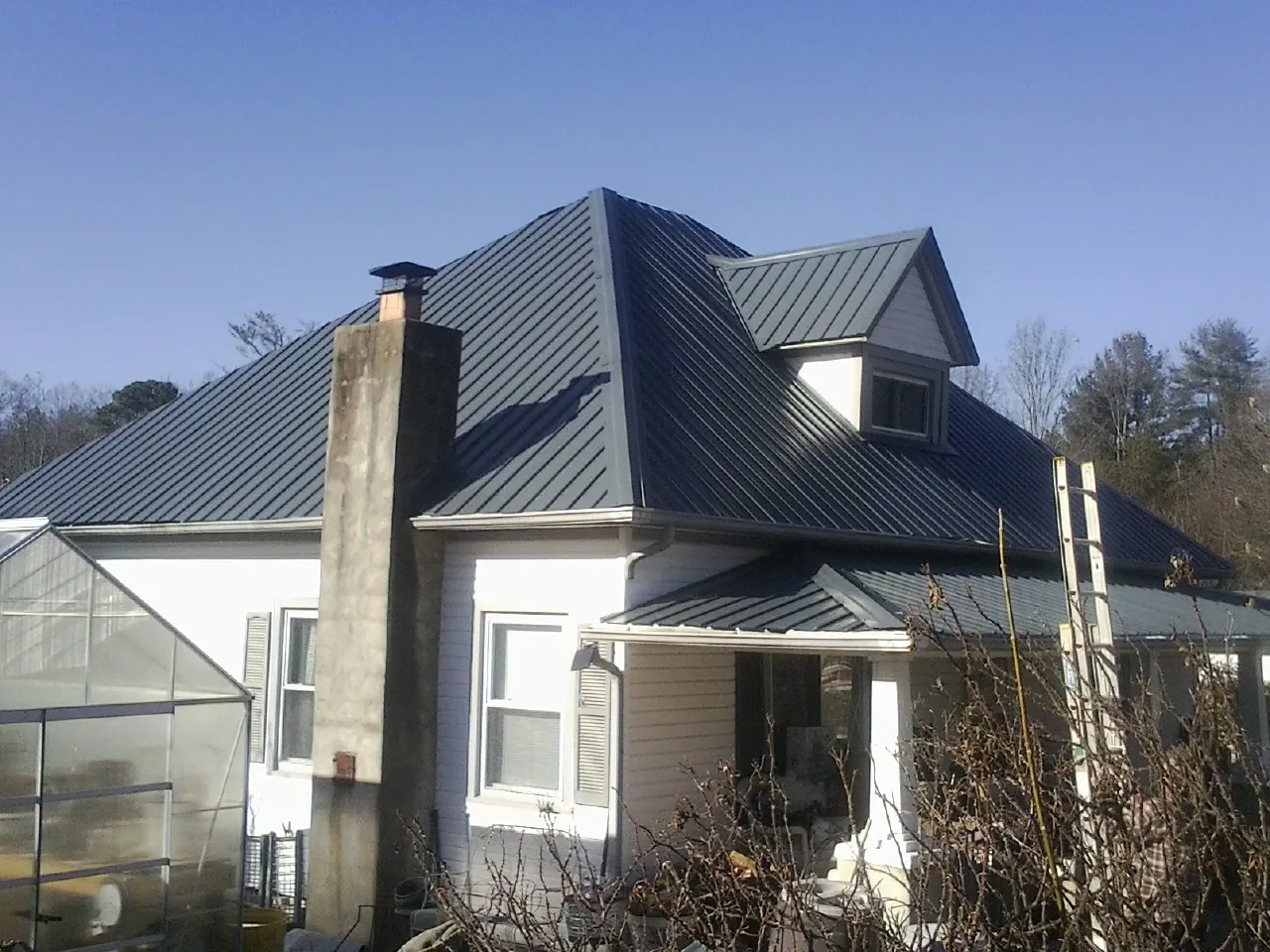 Dark blue standing seam metal roof on a white farmhouse with dormer — Slate & Tile Roof Repair by Roofing Brothers in Venus