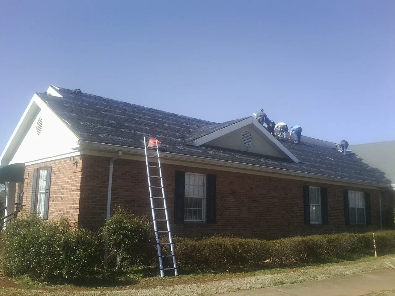 Crew tearing shingles off a brick ranch roof with a ladder set — Metal Roof Repair work by our crew in Venus