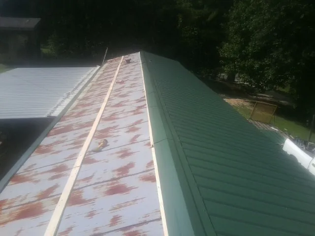 Old rusted panels beside newly installed green metal roofing — Wind Damage Roof Repair by Roofing Brothers in Venus