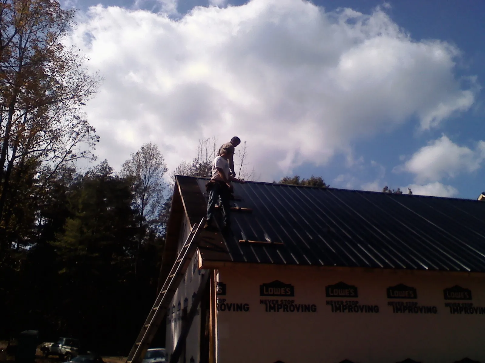 Roofer fastening dark metal panels high against a cloudy sky, from a Roof Inspection job in Venus