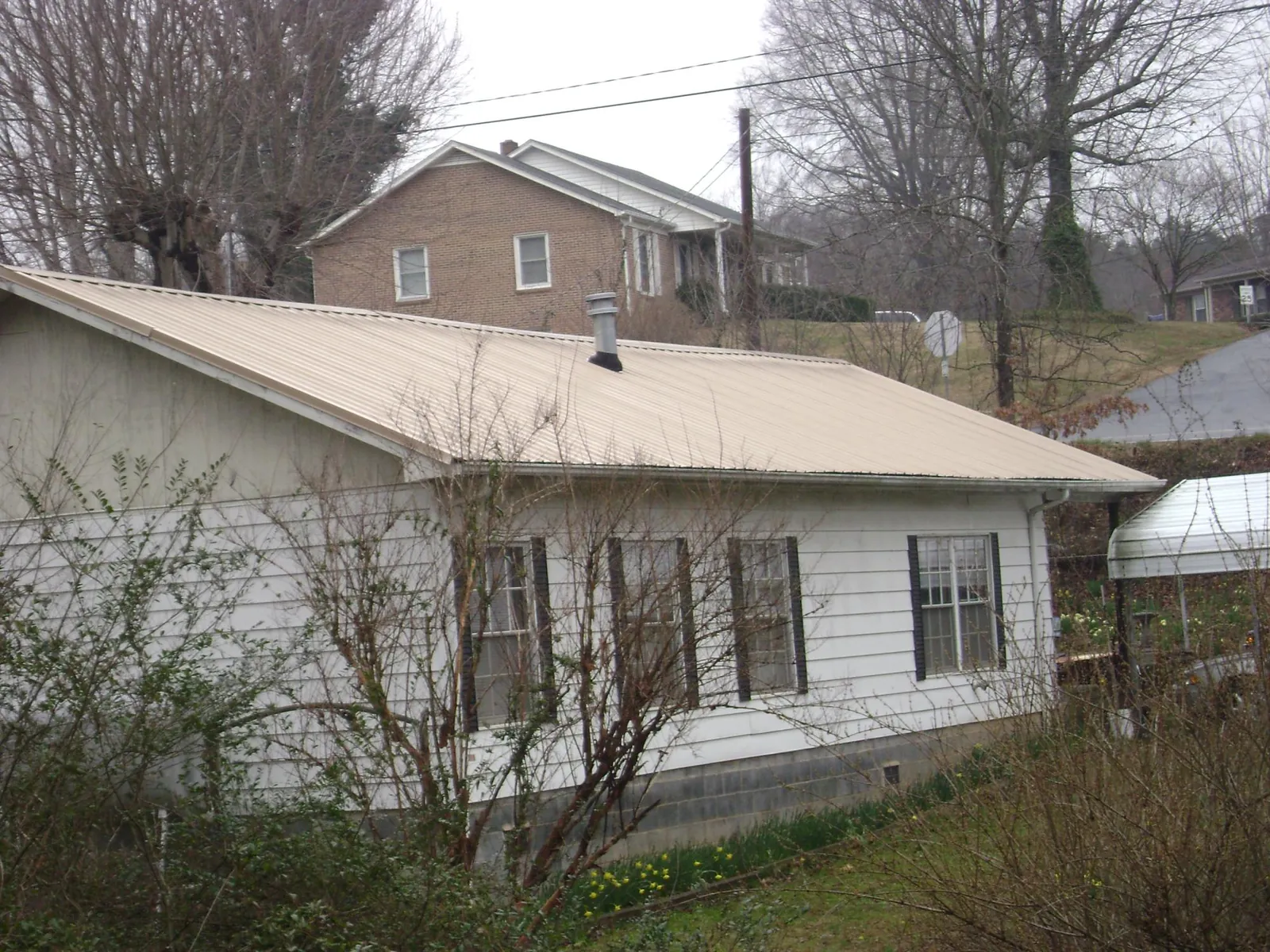 Tan metal roof on a white sided house set into a hillside — Commercial Roofing by Roofing Brothers in Venus